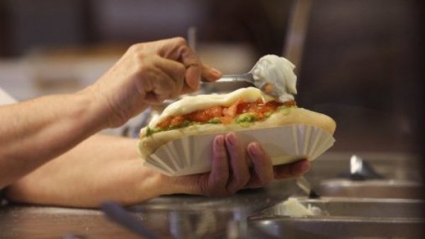<p>Persona preparando un completo italiano en el día del completo.</p>Día del completo: guía completa de promociones y ofertas

