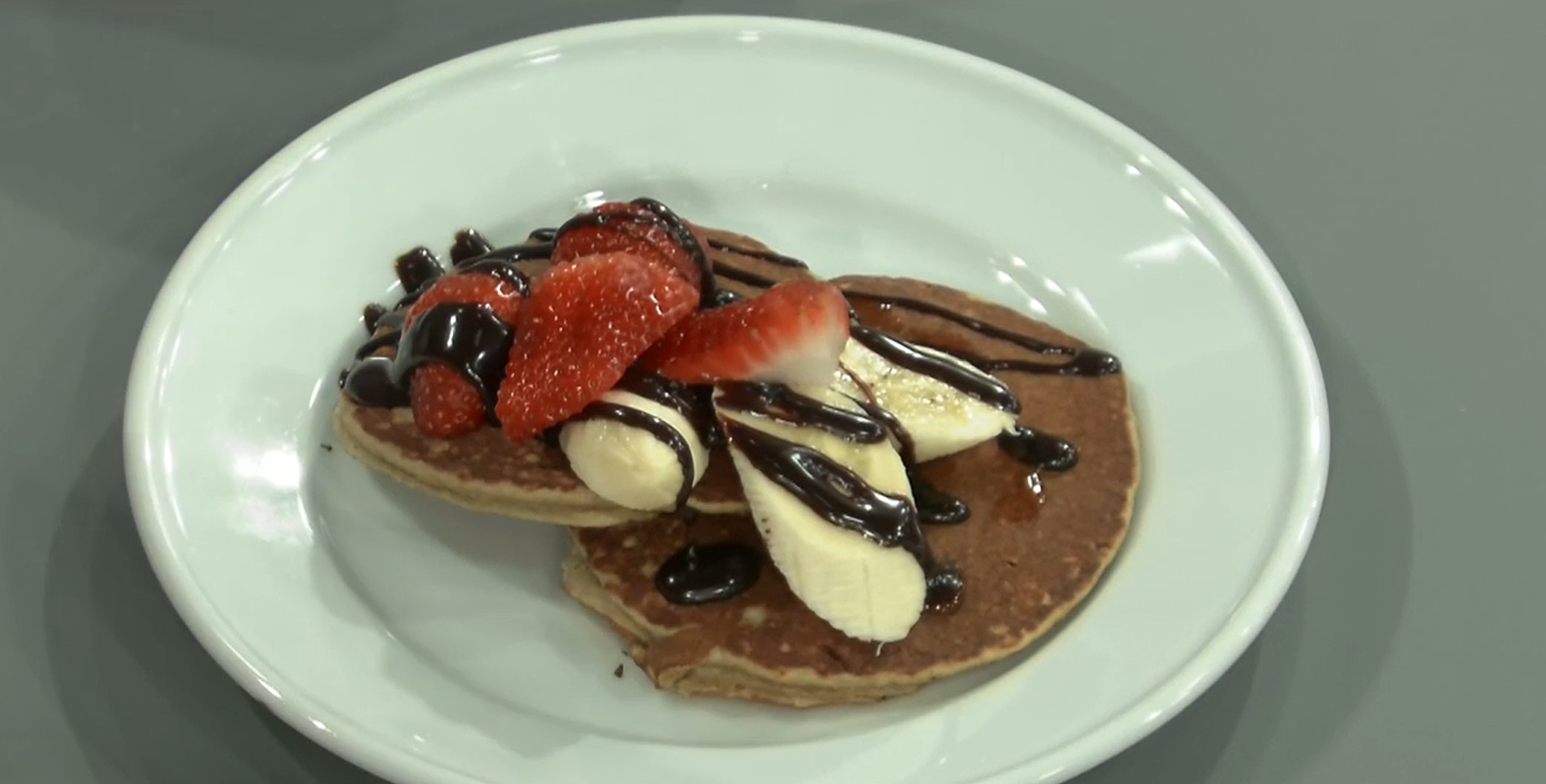 Panqueques en un plato con frutillas y chocolate.