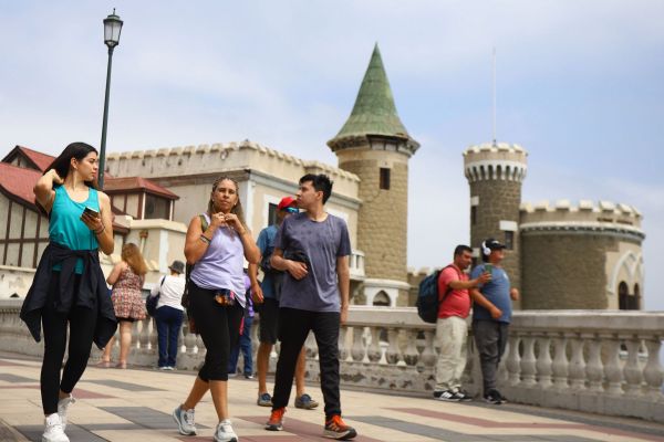 personas caminando por la costanera de viña del mar con castillo de fondo