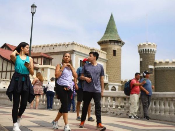 personas caminando por la costanera de viña del mar con castillo de fondo